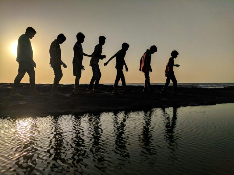 group of children walking near body of water silhouette photography